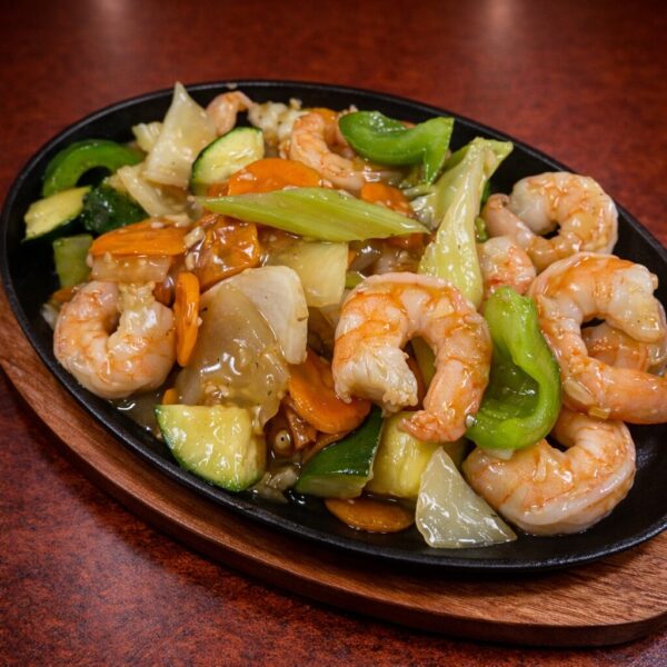 Sizzling shrimp stir-fry with sliced carrots, zucchini, and green peppers served on a hot cast iron platter