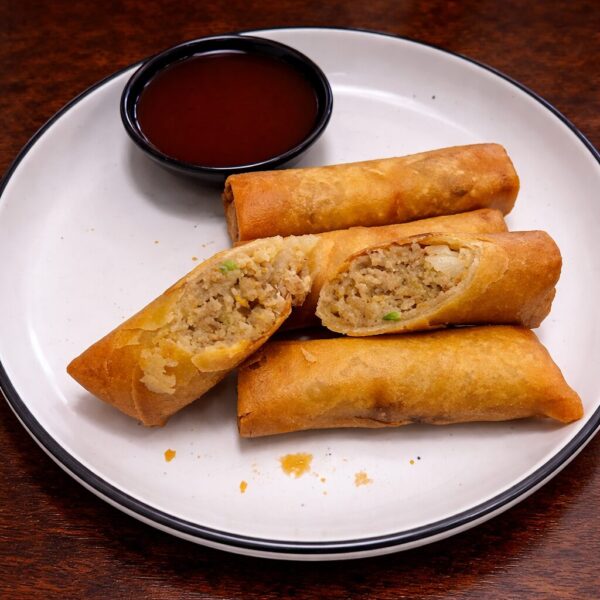 Crispy fried egg rolls served with a side of dipping sauce on a white plate