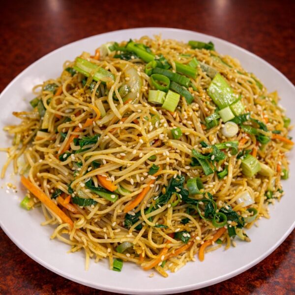 A plate of vegetable stir-fried noodles topped with sesame seeds and chopped green onions